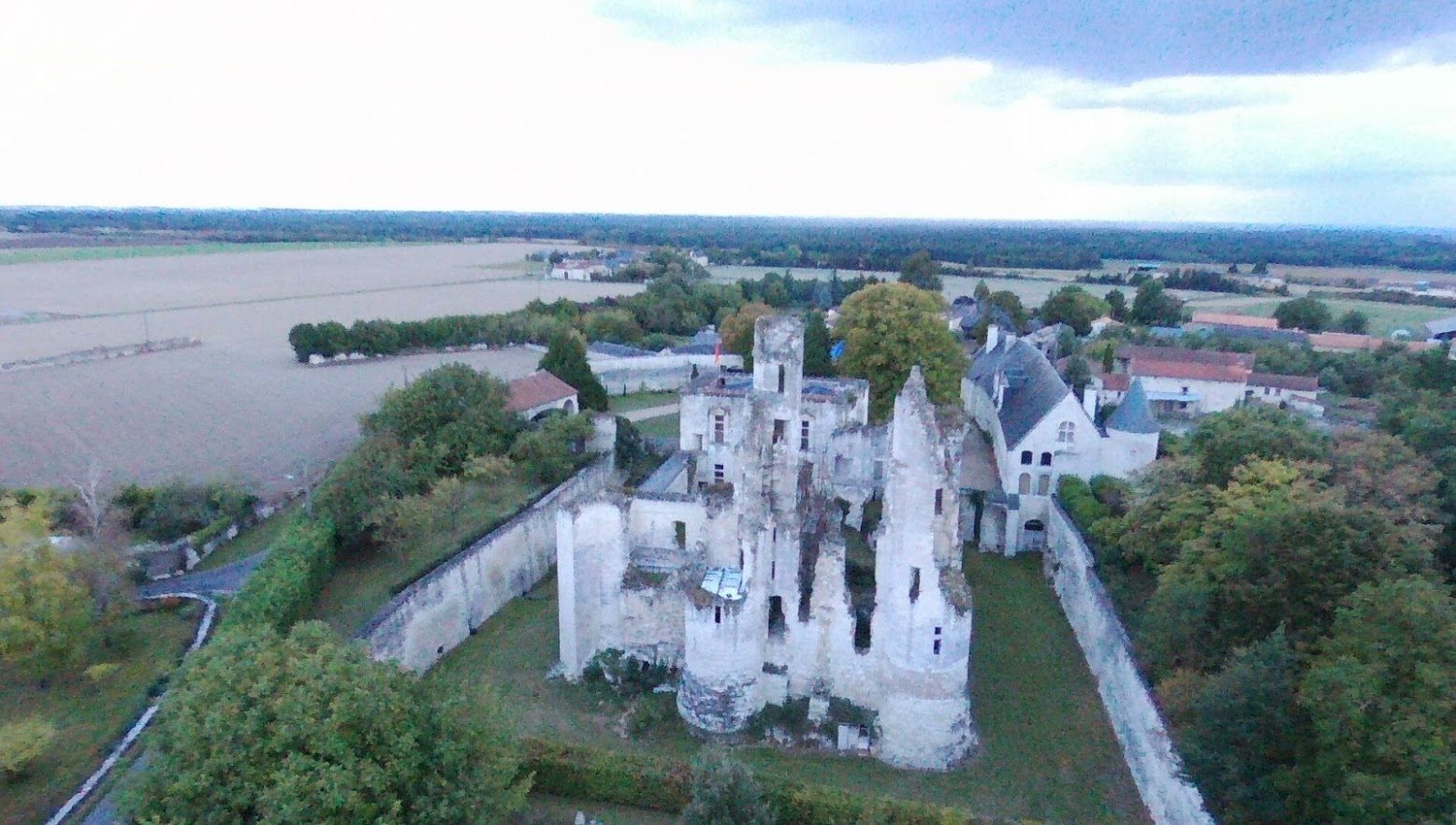 Vue aérienne depuis le nord-est : les deux tours ruinées du château fort au premier plan, la douve de part et d'autre, le châtelet et le long bâtiment derrière.