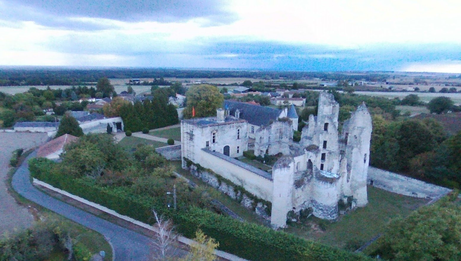 Vue aérienne depuis le sud-est : le châtelet, le long mur d'enceinte de la haute cour terminé par une tour ronde, la douve au pied, les ruines derrière.