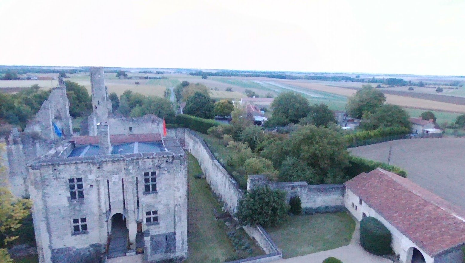 Le châtelet vu de face et d'en haut : porte charretière, pont-levis, fenêtres à meneaux, contreforts, terrasse ; mur d'enceinte et douve à droite.