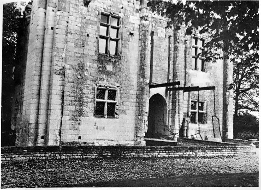 Photo ancienne en noir et blanc de la façade du châtelet : contreforts plats, fenêtres à meneaux, porte avec pont-levis relevé, parapet au premier plan.