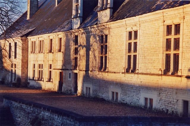 Façade du long bâtiment au soleil couchant : grandes fenêtres à meneaux en croix, lucarnes, mur de pierre blanche.