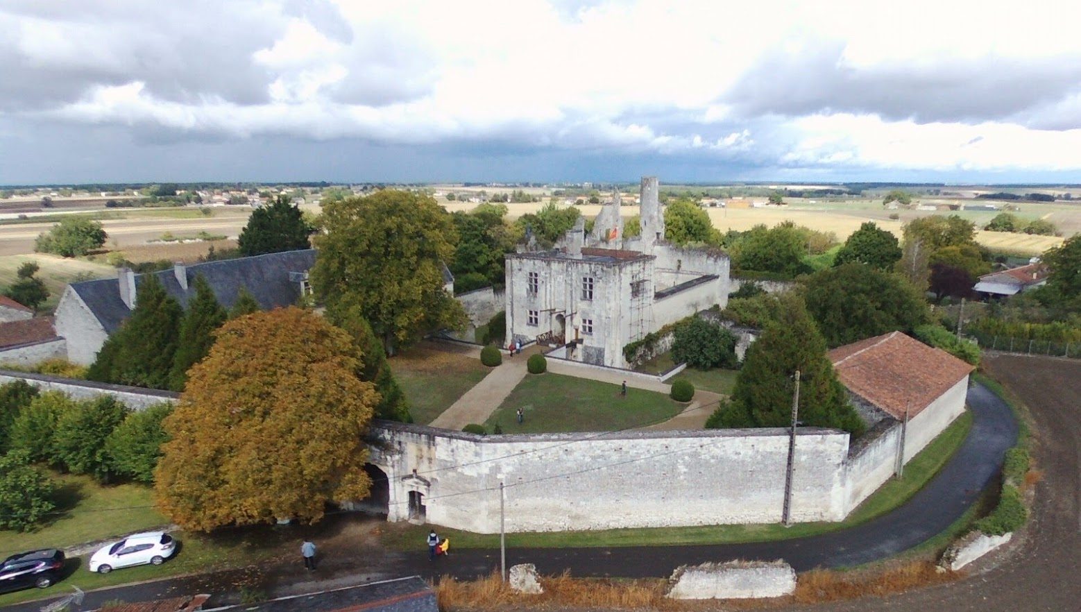 Vue aérienne depuis la route : le portail dans le mur de clôture, la cour d'honneur, le châtelet et les ruines.