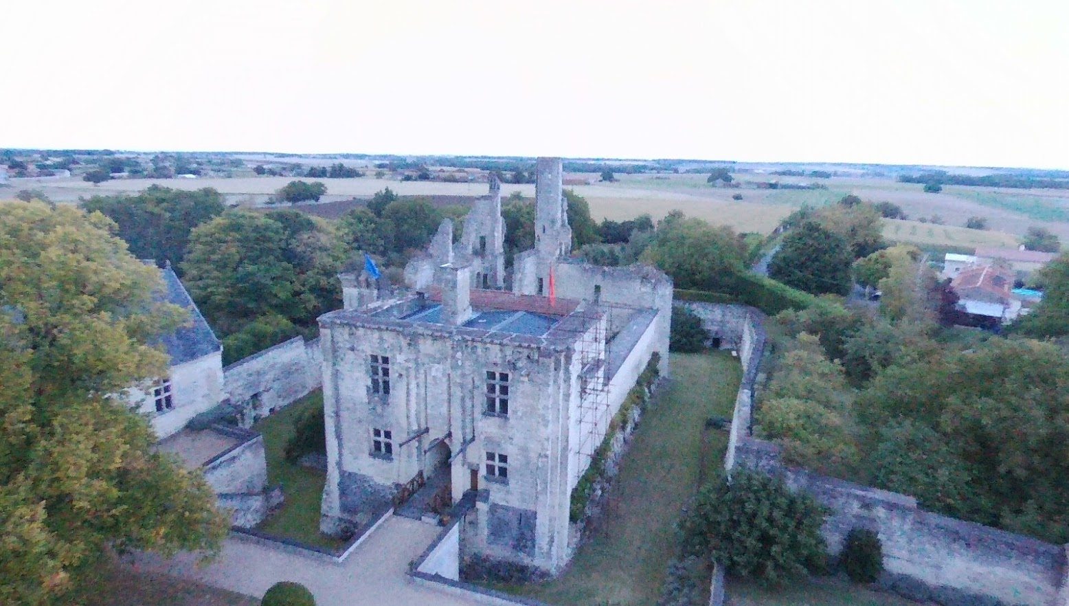 Le châtelet vu du sud : bâtiment massif à contreforts et fenêtres à meneaux, terrasse, tours ruinées derrière, douve à droite.