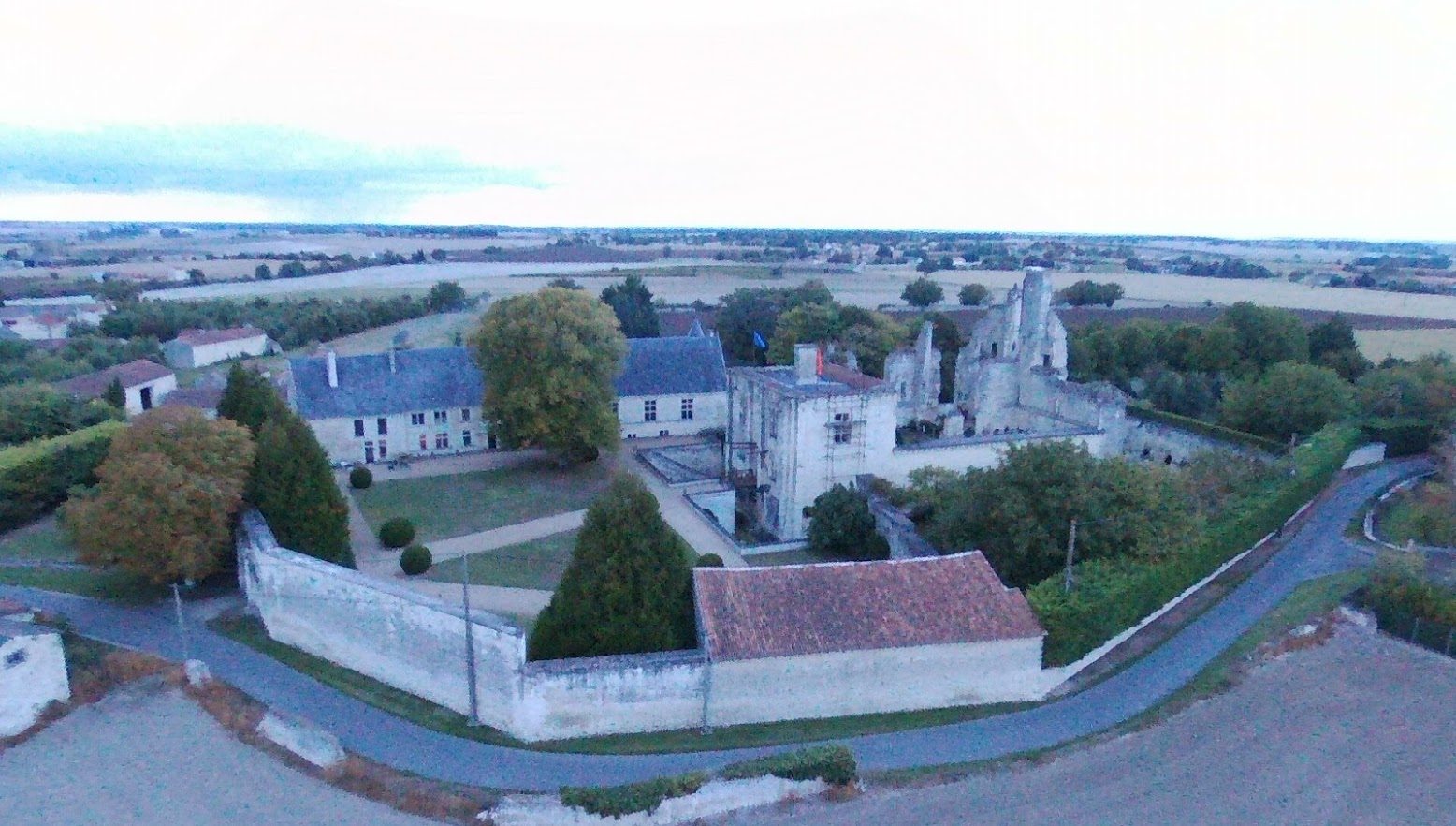 Vue aérienne depuis le sud-ouest : long bâtiment à gauche, châtelet au centre, ruines derrière, dépendance et mur de clôture au premier plan.
